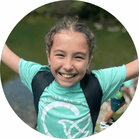 A smiling school age child with her arms spread out during summer camp at Celebree School of Bel Air.