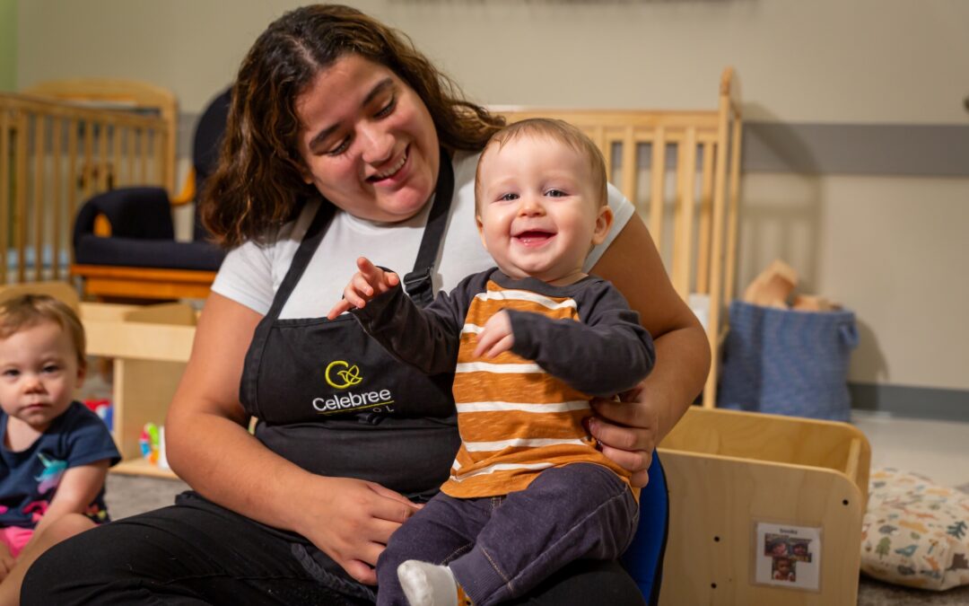 Teacher holding and smiling with an infant during playtime at Celebree School, creating a warm and nurturing classroom environment.