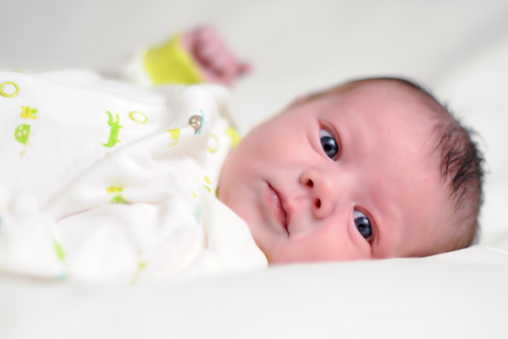 A young baby wearing a cute onesie while staring with wide blue eyes. 