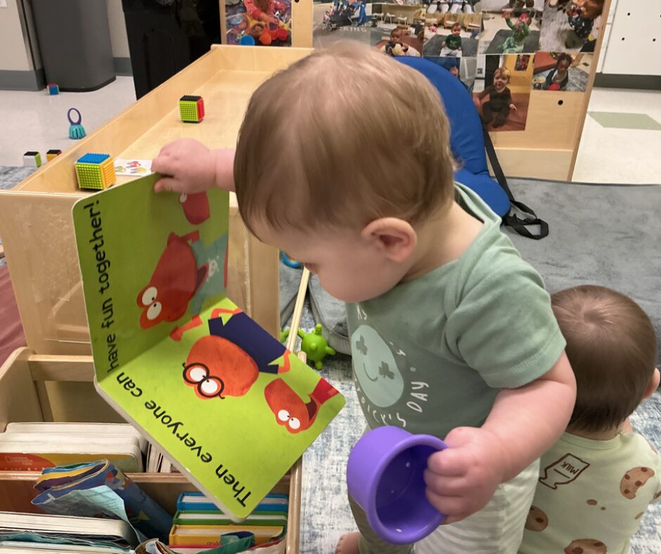 Toddler exploring a board book in a classroom reading area, encouraging early literacy development, curiosity, and independent learning