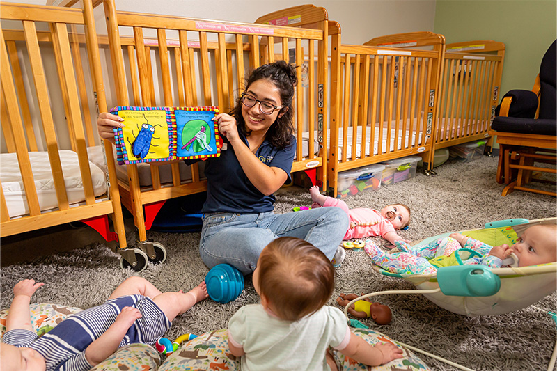Teacher reading soft book to group of infants on ground level