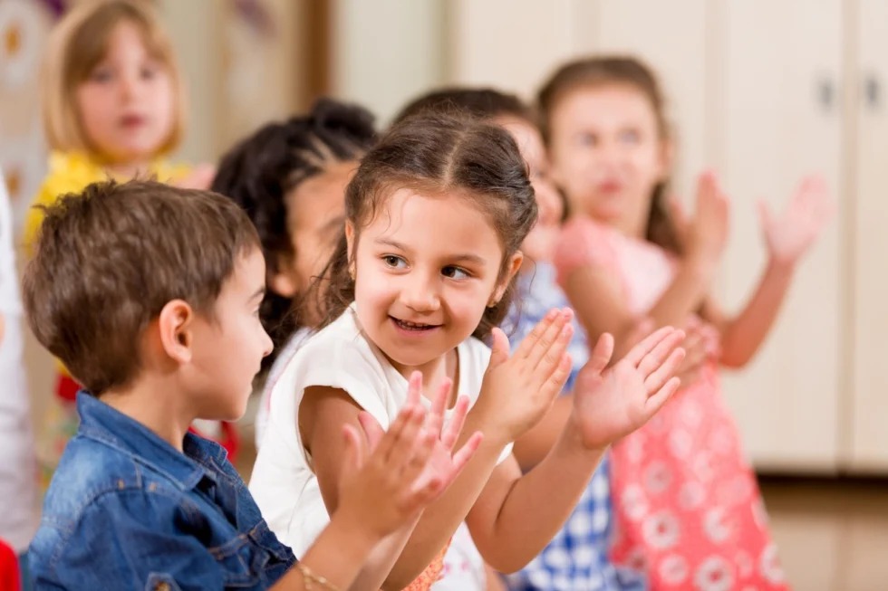A group of children in a Celebree School of Ellicott City classroom, joyfully clapping their hands together, showing excitement and engagement.