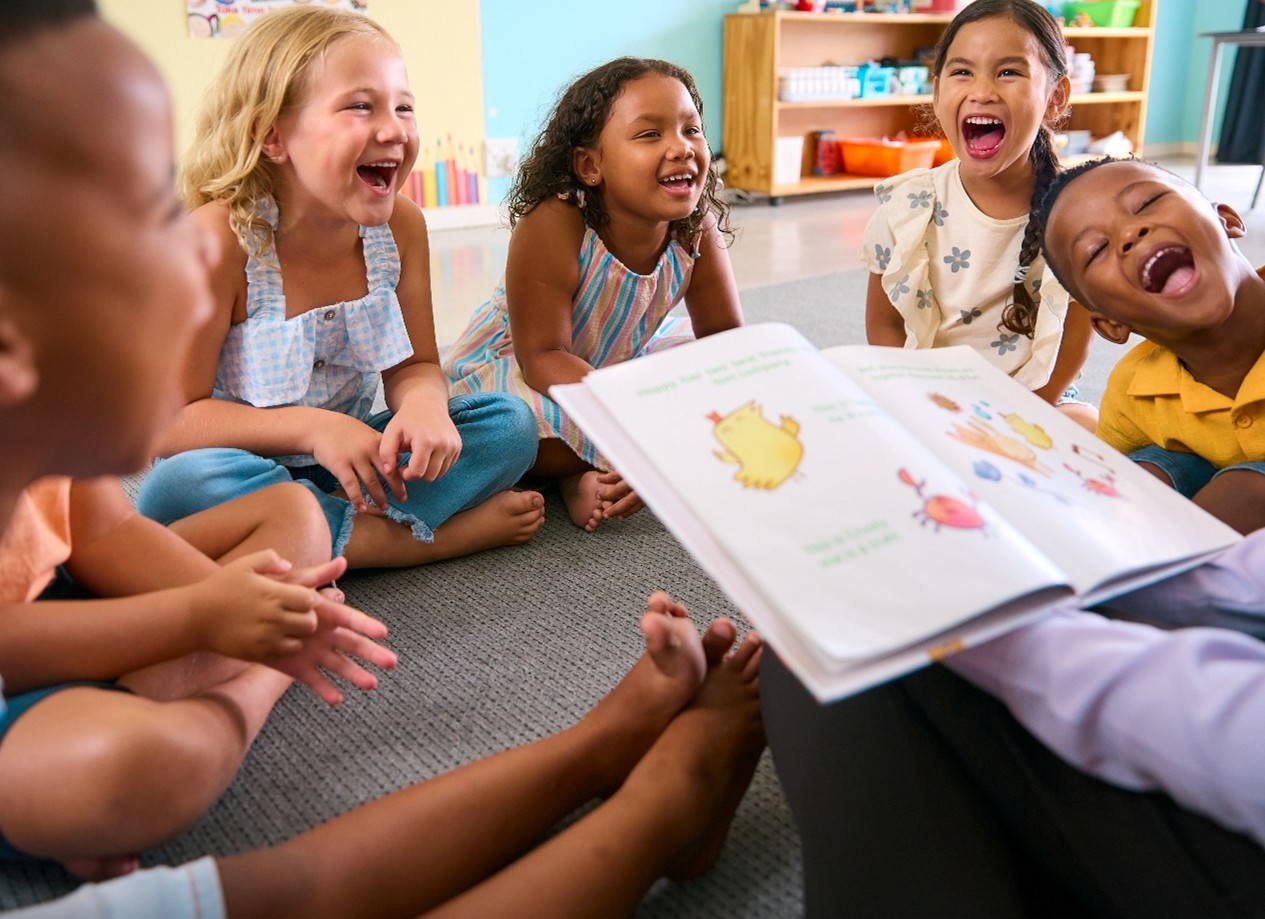 Pre-K students during circle time smiling while the teacher reads a book. 