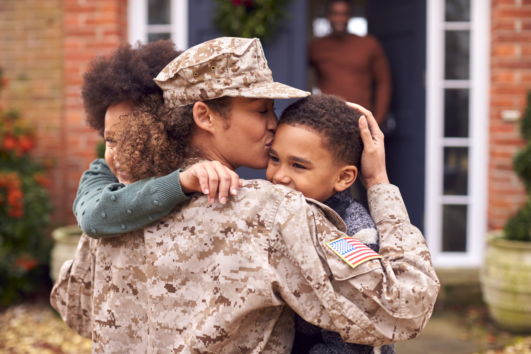 American Female Soldier In Uniform Returning Home To Family On Hugging Children Outside House American Female Soldier In Uniform Returning Home To Family On Hugging Children Outside House