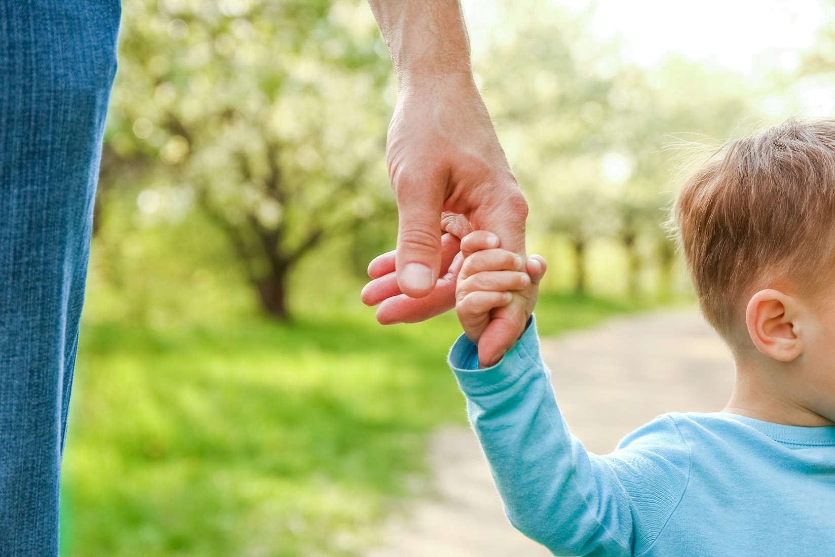 Close up image of a dad holding hands with his little boy while walking. 