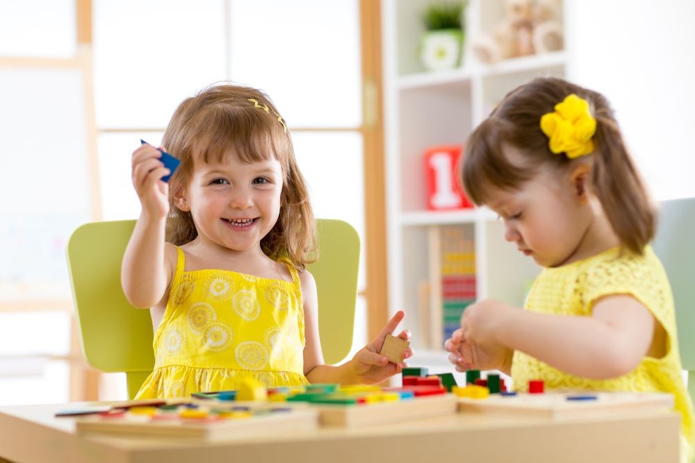 Two little girls wearing yellow dresses doing a craft at a table during a day at child care.