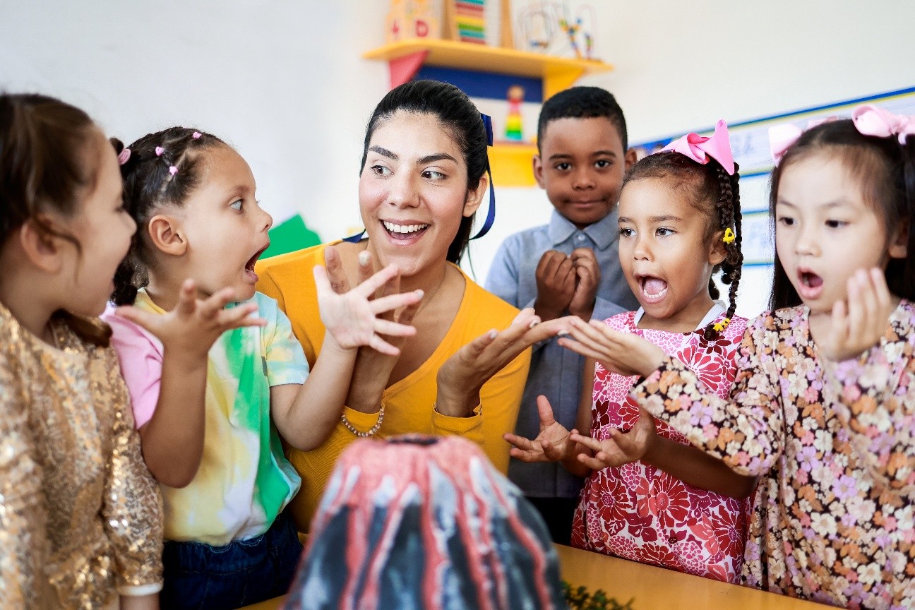 1 June A smiling woman with long brown hair hugs three diverse young children at a table, at Celebree.