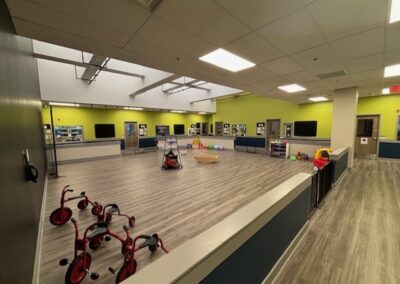 Spacious indoor playroom with tricycles and various play stations.