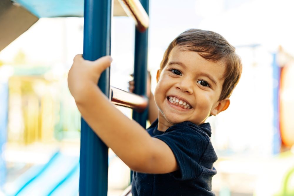 Dallas NorthPark’s Preschool A little boy smiling and climbing a ladder on a playground.