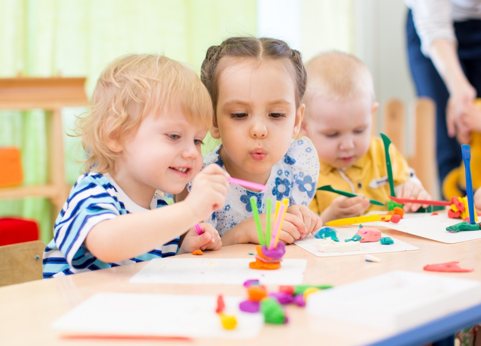 Three toddlers sitting at a table doing a craft while being cared for in a child care environment