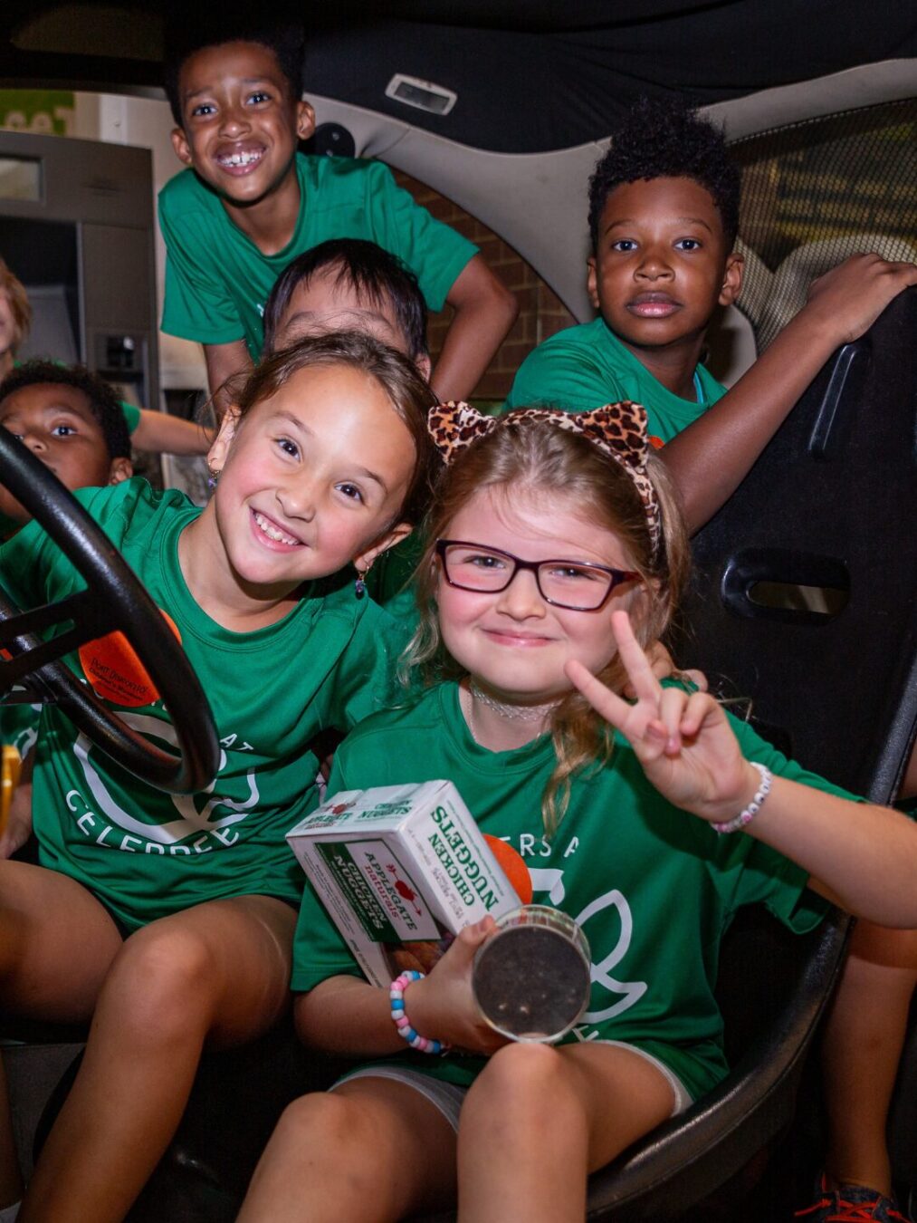 Smiling kids gathered together in a vehicle wearing matching green shirts on their way to a fun summer camp activity.