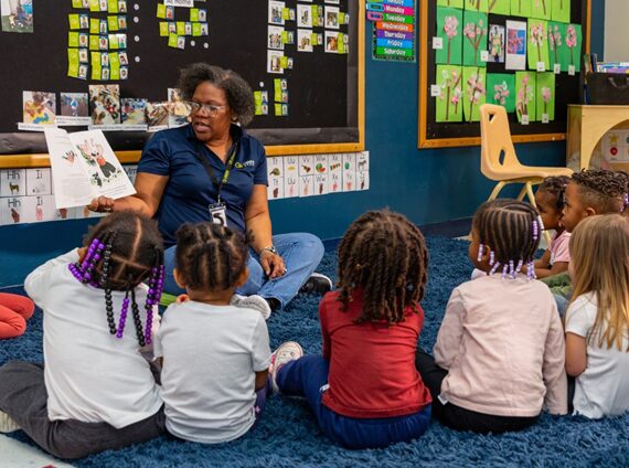 Day Care A Celebree School teacher reads a picture book to a group of young children seated in a colorful classroom during story time.<br />