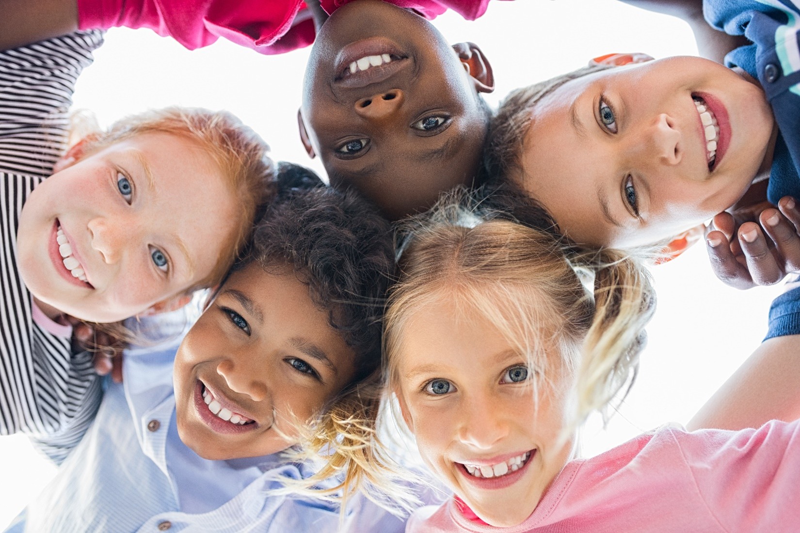 Five smiling kids with their heads together looking down.