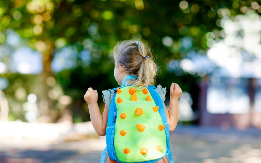 Image Alt Tag: The back side of a confident preschool girl wearing a backpack that resembles a dinosaur.