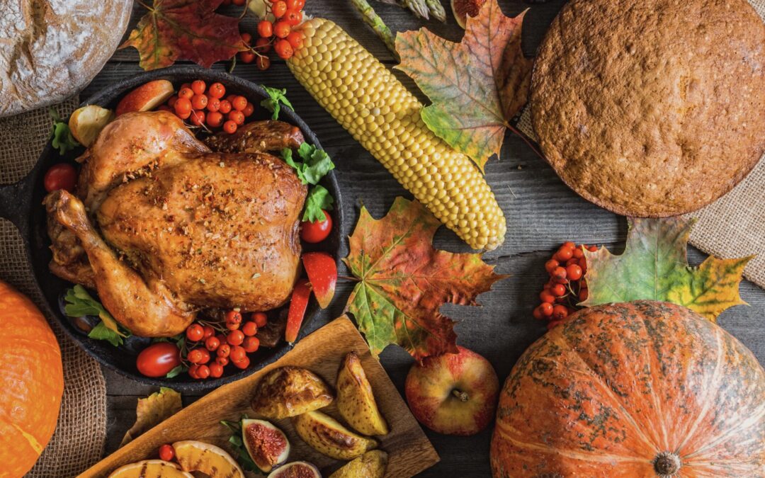 Roasted turkey surrounded by traditional Thanksgiving foods, including corn, pumpkin, apples, and autumn leaves on a rustic wooden table.