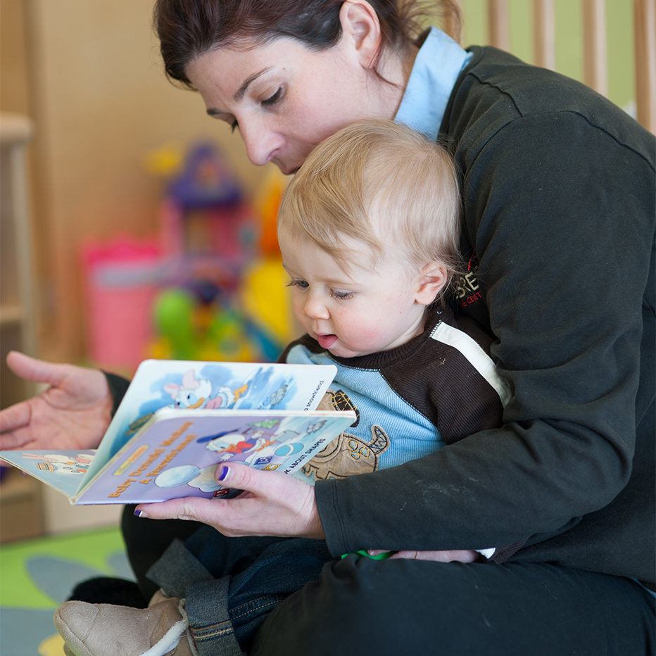 A teacher reading a book to a baby at infant child care in Tysons.