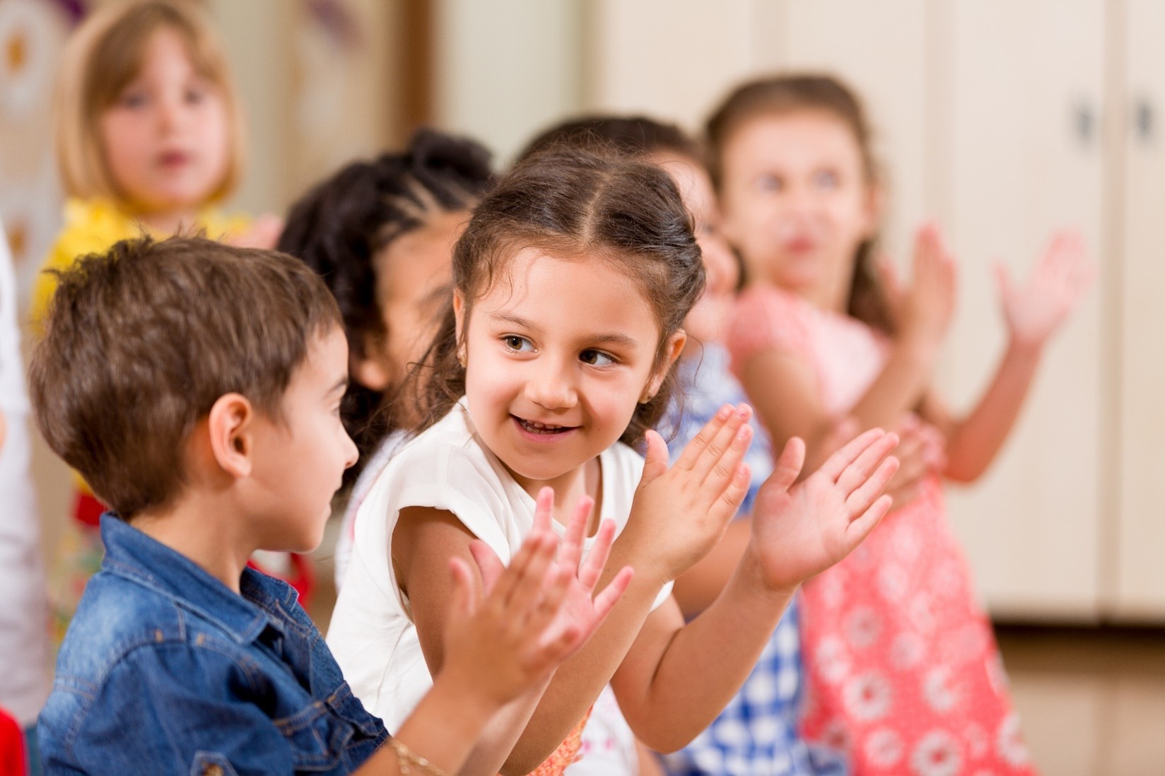 Celebree School A group of children in a classroom, joyfully clapping their hands together, showing excitement and engagement.