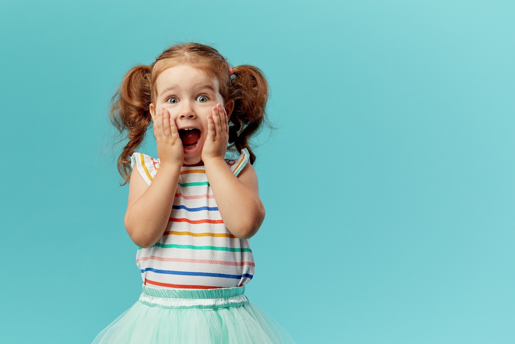 A young girl with pigtails, a striped shirt, and a light blue tutu, looking surprised and happy against a blue background.