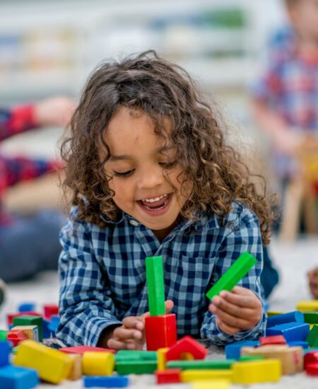 Little preschooler boy with curly brown hair playing with rainbow blocks in a classroom.