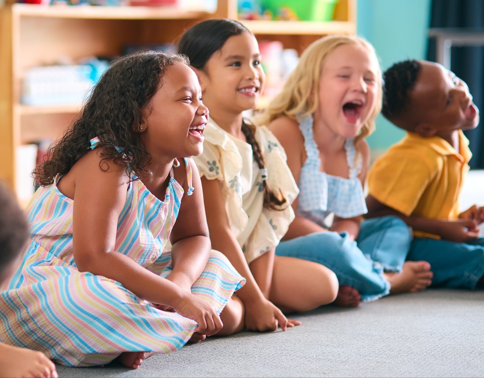Four children in pre-K sitting in a row during circle time and laughing.