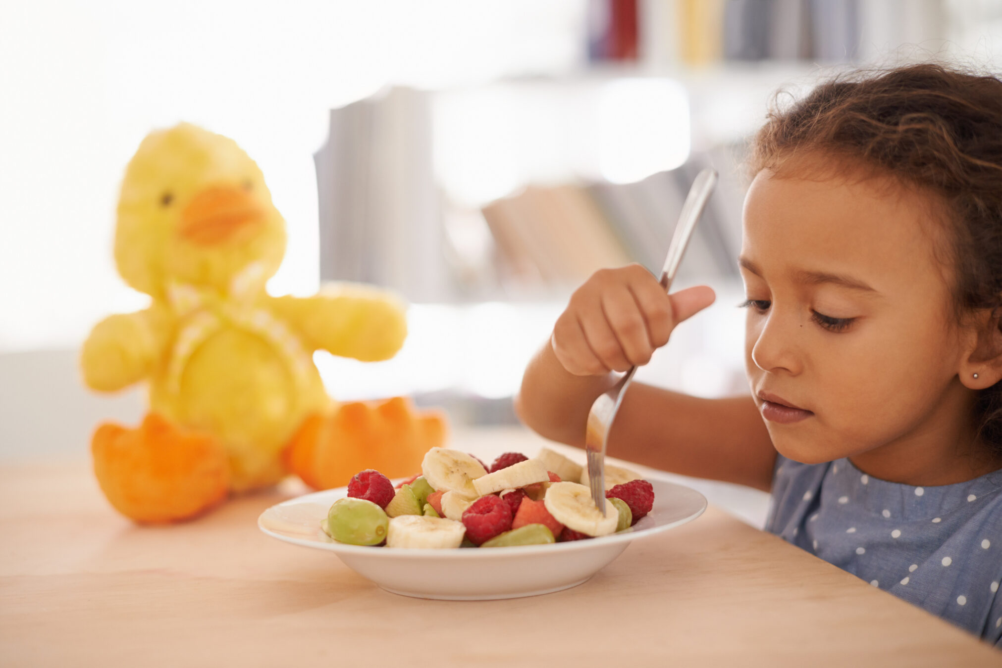 Young child eating a healthy fruit snack with bananas, grapes, and berries, promoting healthy eating habits and nutrition for early childhood development.