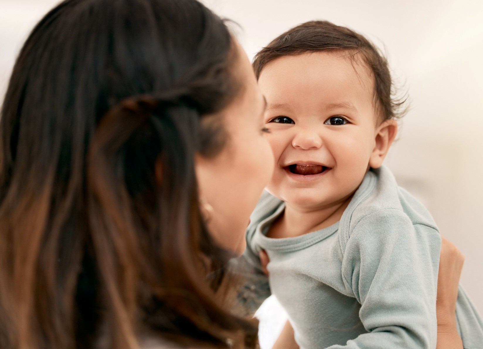The back of a mom’s head while she holds her infant up and the infant has a big smile.
