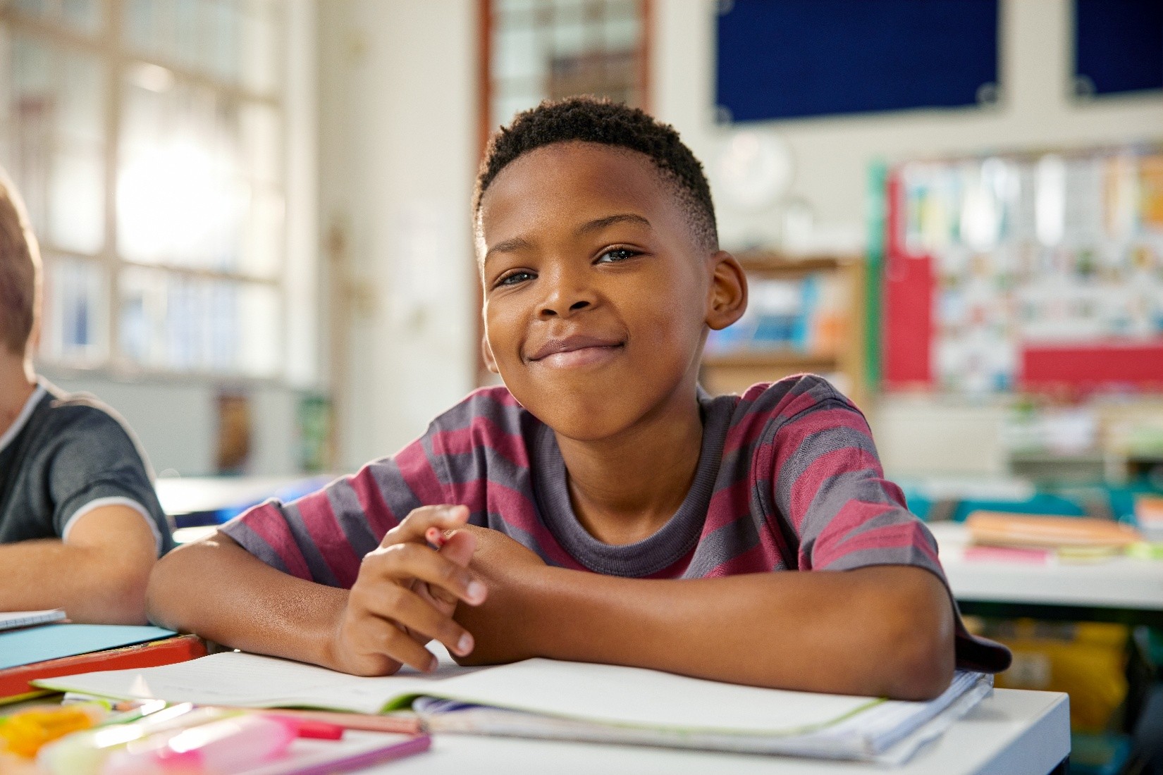 A young boy sitting at a desk and smiling while he is doing his homework after school.