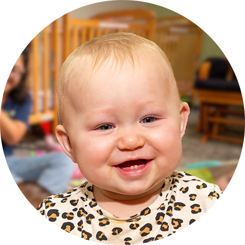 A smiling baby with blonde hair in the infant classroom.