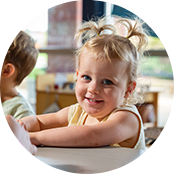 A young toddler with blonde hair in two tiny pigtails and a big smile.