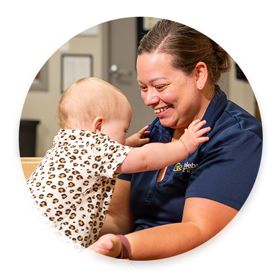 A Celebree School of Grandville caregiver with an infant using her to stand up and balance.